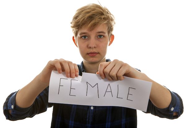 Homme trans qui déchire une pancarte "female"